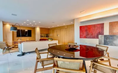 Sala de jantar com mesa redonda em laca, cadeiras de palhinha e quadros assinados